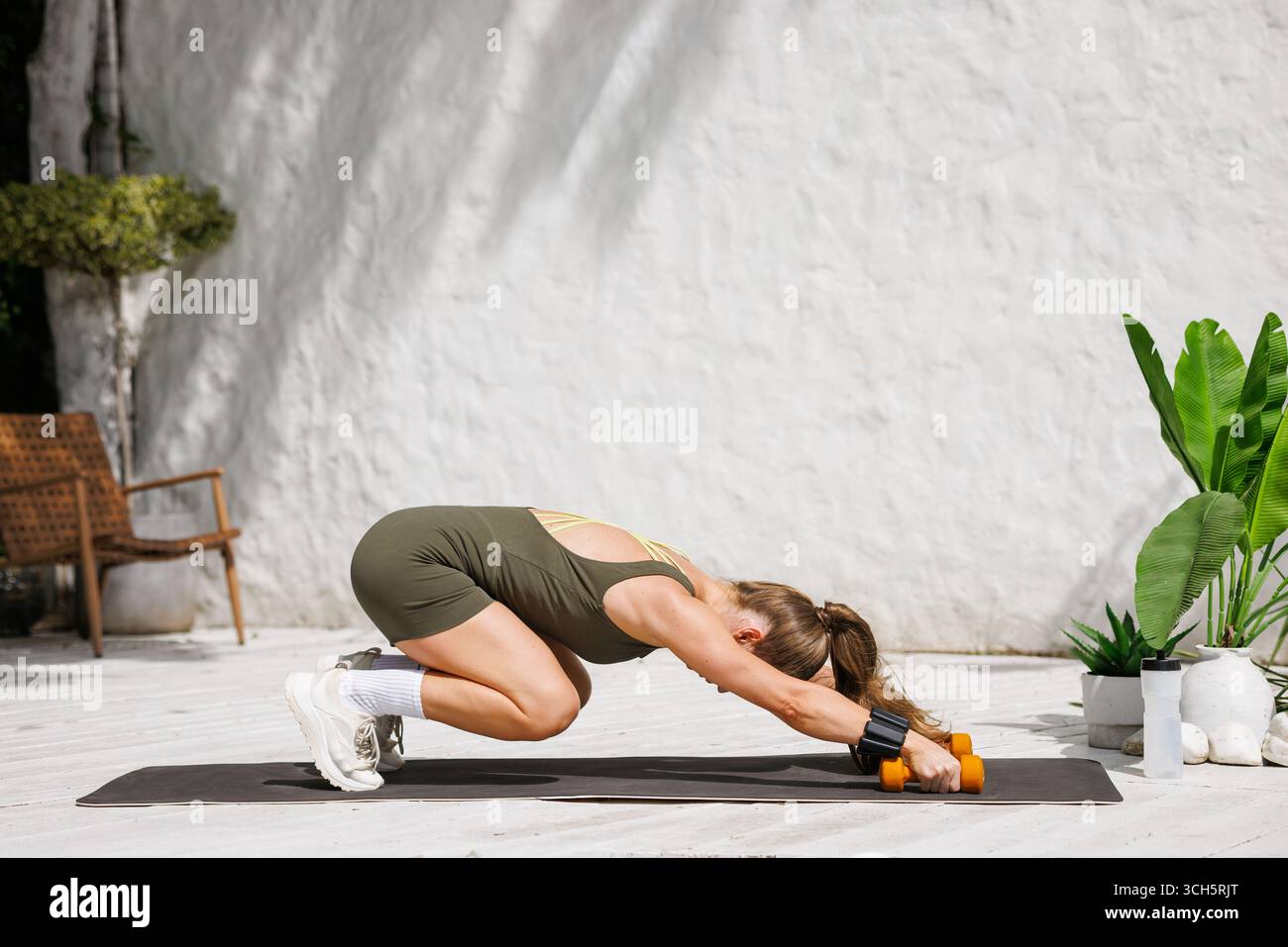 La donna si allunga su un tappetino con manubri e pesi per le braccia all'aperto scena moderna per il recupero, la mobilità durante il riscaldamento e il basso contenuto di resistenza agli urti Foto Stock