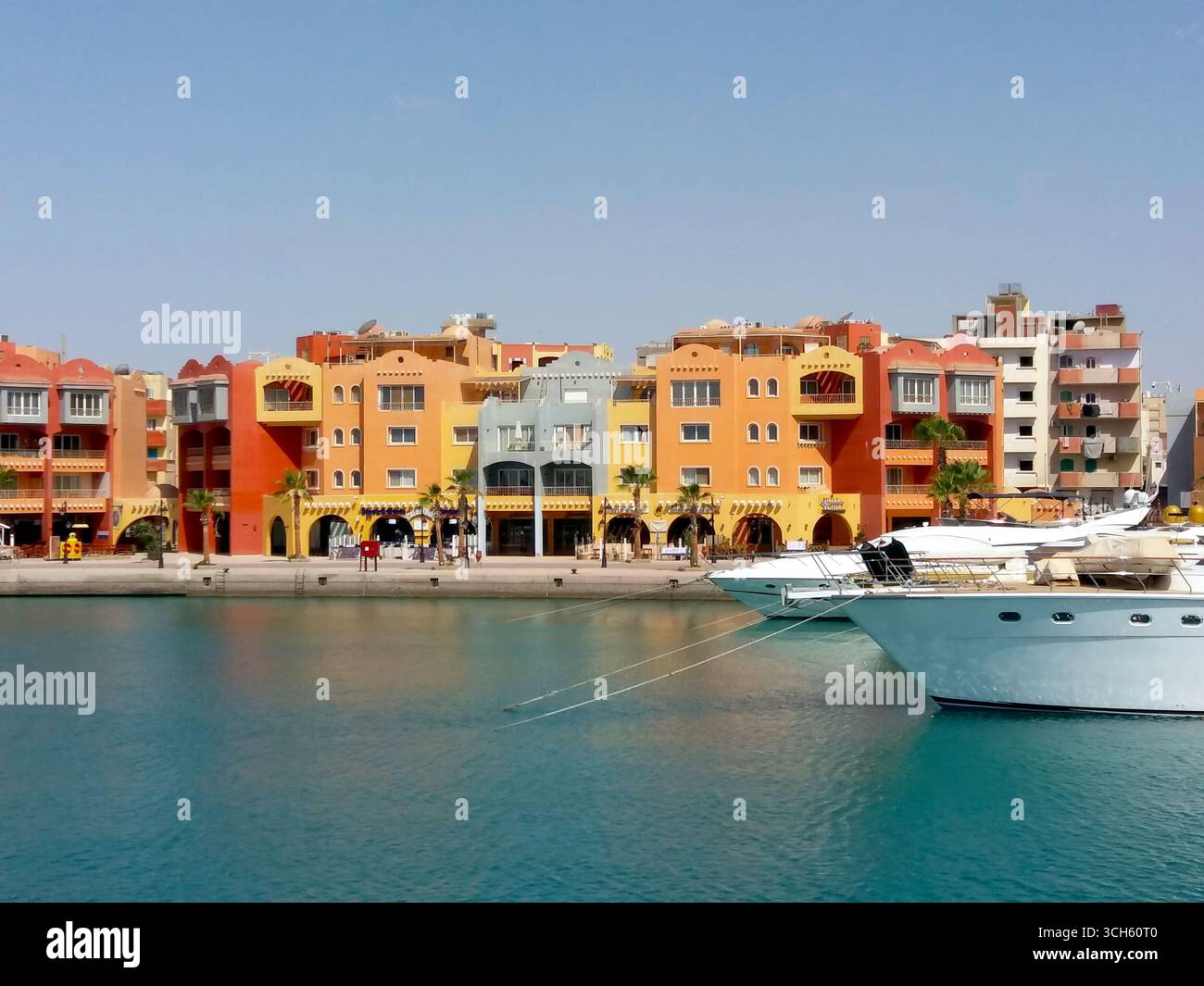 I visitatori passeggiano lungo il lungomare della baia di Hurghada, in Egitto, ammirando gli edifici vibranti e gli yacht turistici ormeggiati contro un cielo limpido. Foto Stock