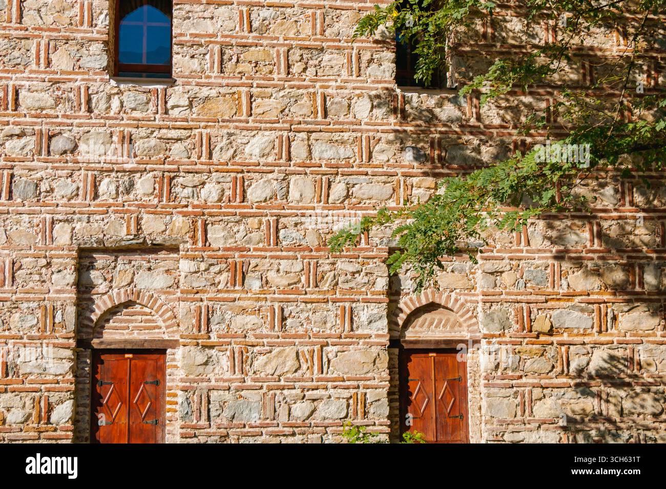Intricati lavori in pietra e porte in legno creano un'allettante facciata di questo edificio storico, abbracciato dalla natura sotto il caldo bagliore del sole pomeridiano Foto Stock