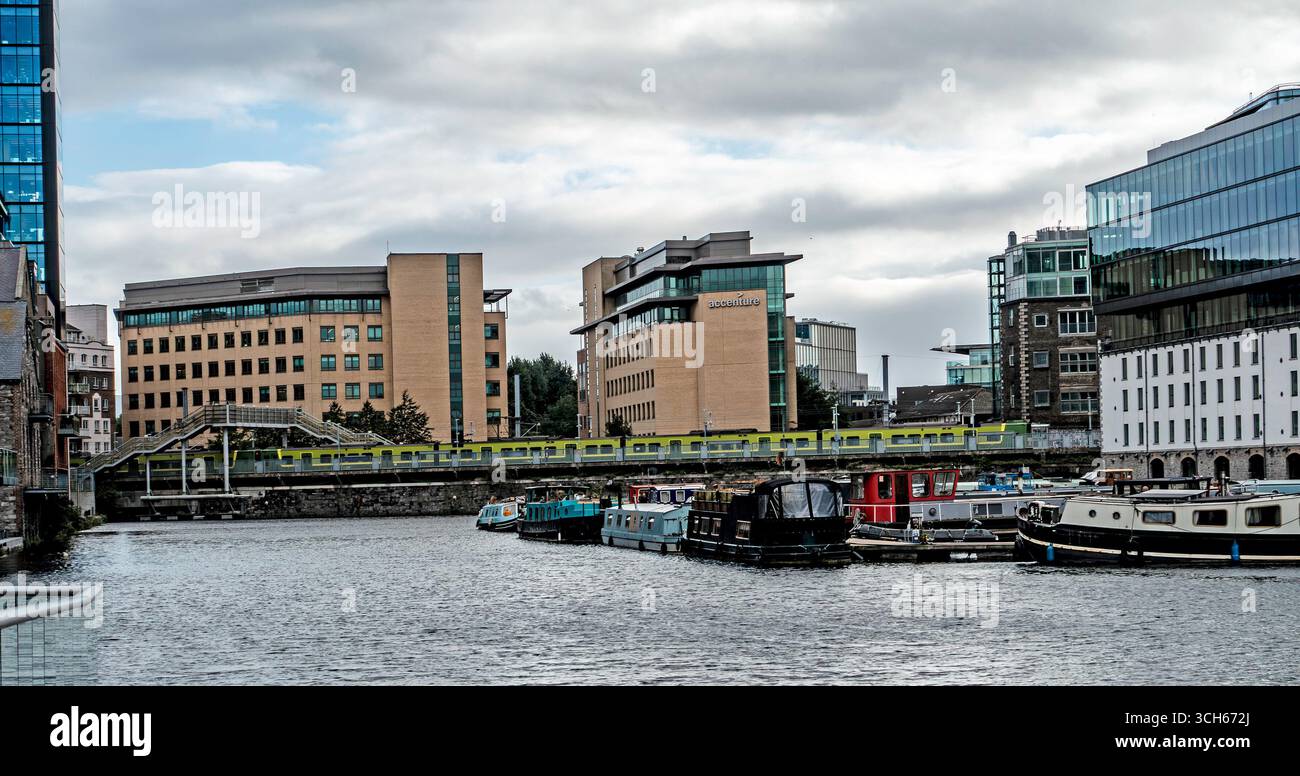 Grand Canal Quay, Dublino, Irlanda, con case galleggianti ormeggiate, uffici moderni, Accenture e un treno DART che attraversa il ponte ferroviario sullo sfondo Foto Stock