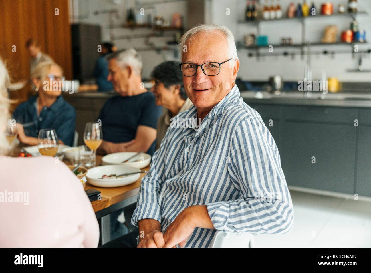 Ritratto di un anziano sorridente seduto a pranzo con gli amici dopo la lezione di cucina Foto Stock