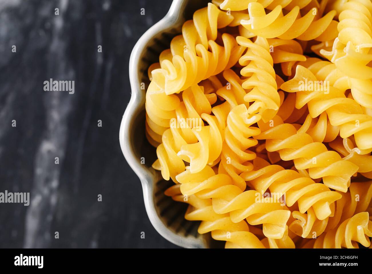 Sfogliare la pasta fusilli in un recipiente di ceramica. Primo piano di spaghetti crudi sul tavolo di marmo. Ingrediente alimentare italiano per cucinare. Consistenza di maccheroni gialli. Foto Stock
