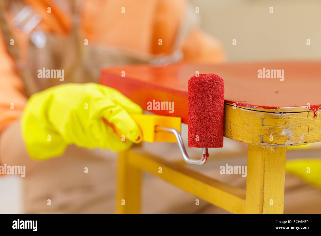 Il rullo in schiuma applica la vernice rossa a una vecchia sedia in legno ristrutturata con il fai da te e il upcycling sostenibile dei mobili a casa Foto Stock