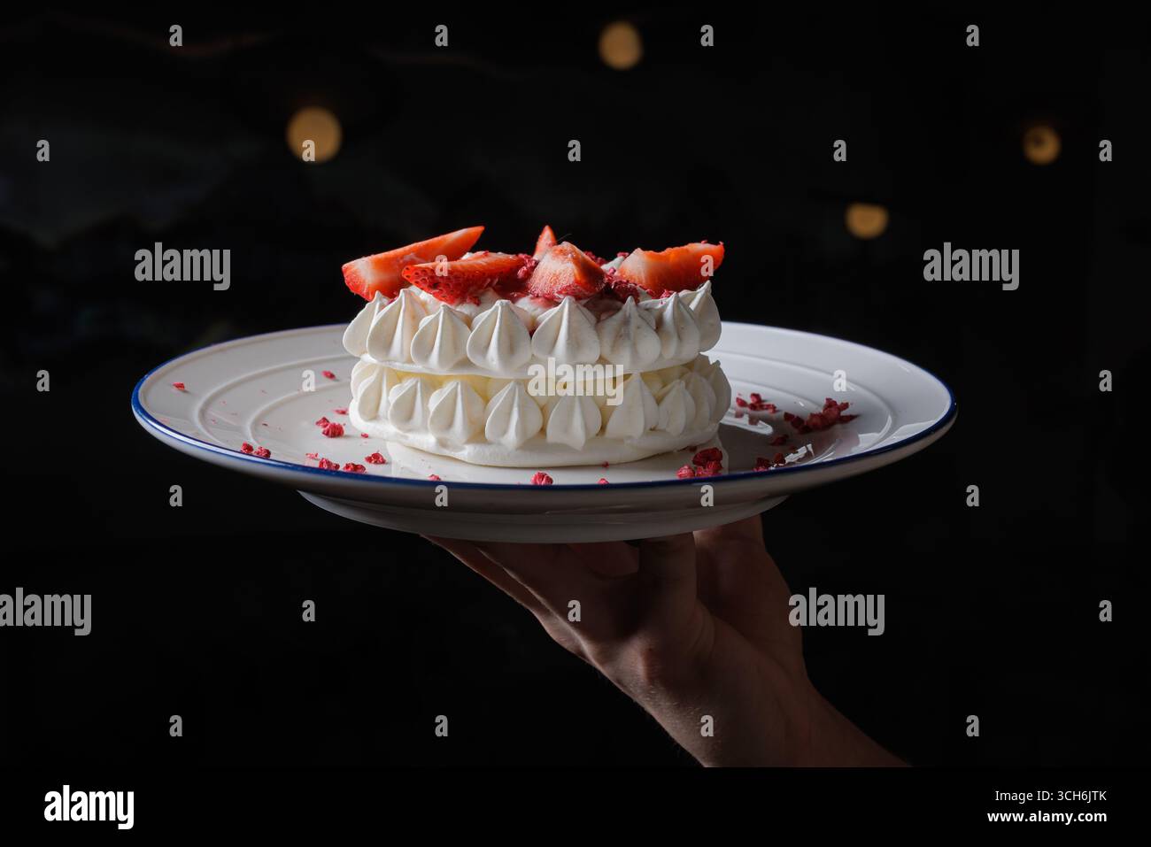 dessert arioso con meringa con crosta delicata e croccante e un centro morbido, e fragole fresche, tenute a mano su uno sfondo scuro Foto Stock