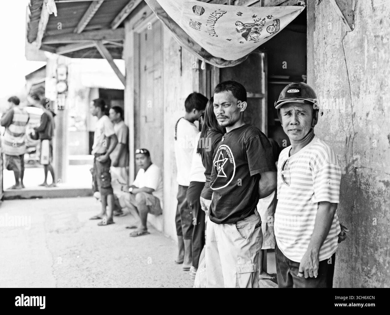 Foto in bianco e nero di gente locale filippina seduta all'ombra lungo una strada a Caramoan, Filippine. Un momento tranquillo della vita di tutti i giorni in un piccolo spazio Foto Stock