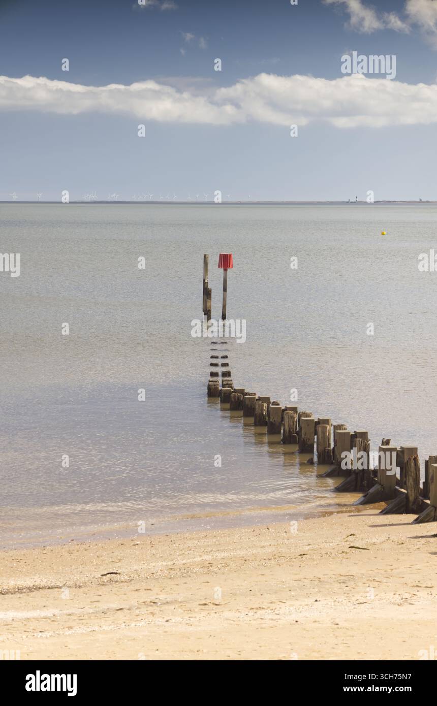 Ammira l'estuario dell'Humber dalla spiaggia, guardando in basso un groyne con un indicatore di navigazione conico rosso sotto un cielo blu con una linea di nuvole Foto Stock