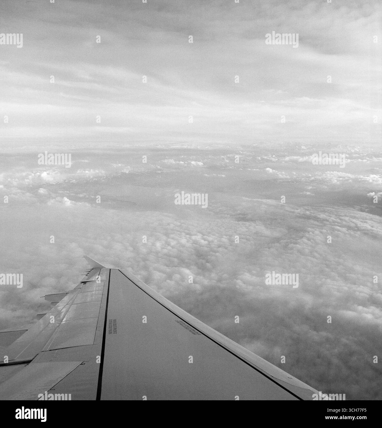 Ala dell'aereo sopra le nuvole: Formato quadrato bianco e nero dal posto vicino al finestrino Foto Stock