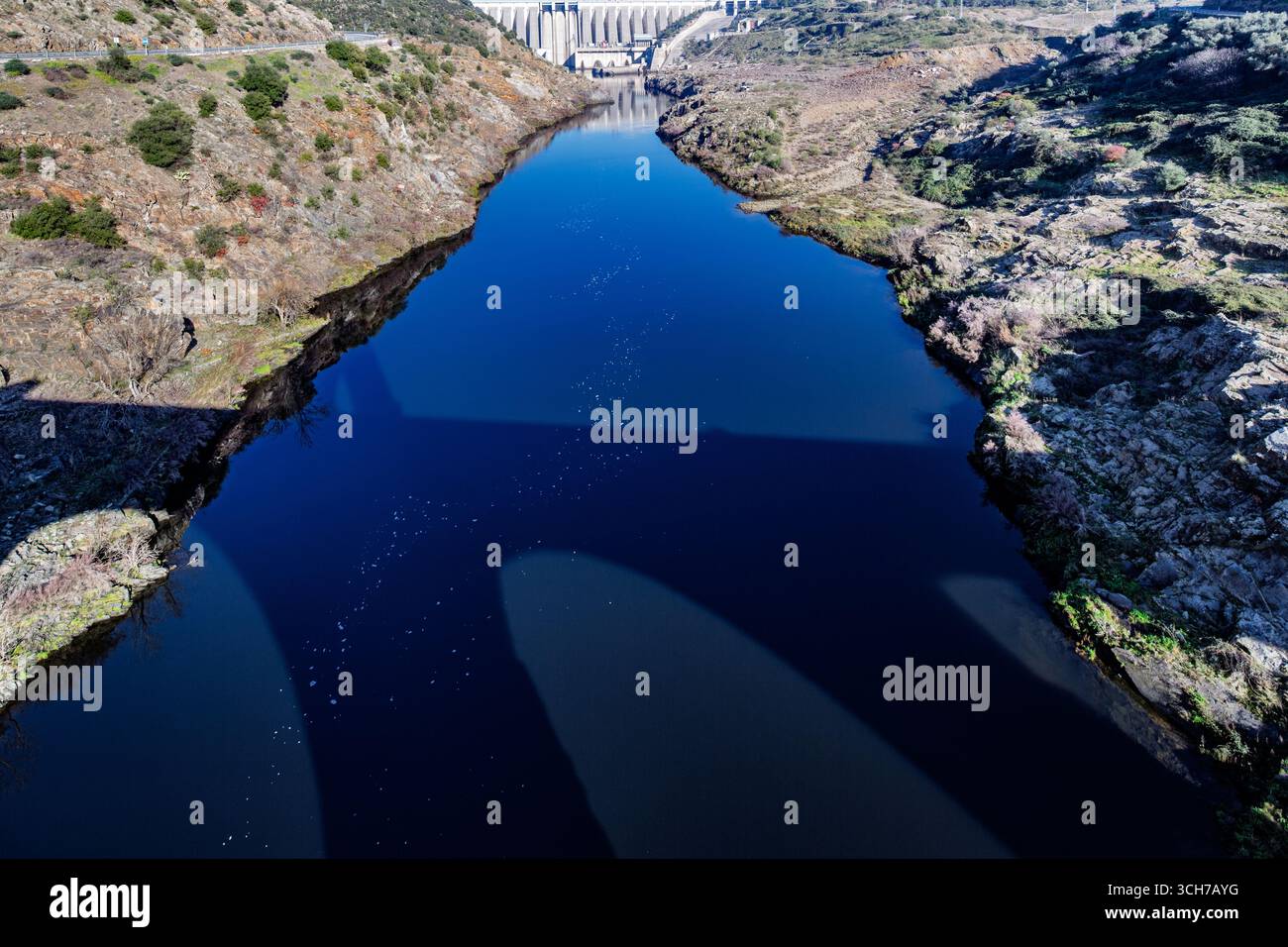 Un ponte romano getta un'ombra sul fiume Tago, con la diga di Alcántara sullo sfondo, evidenziando le meraviglie dell'ingegneria. Foto Stock