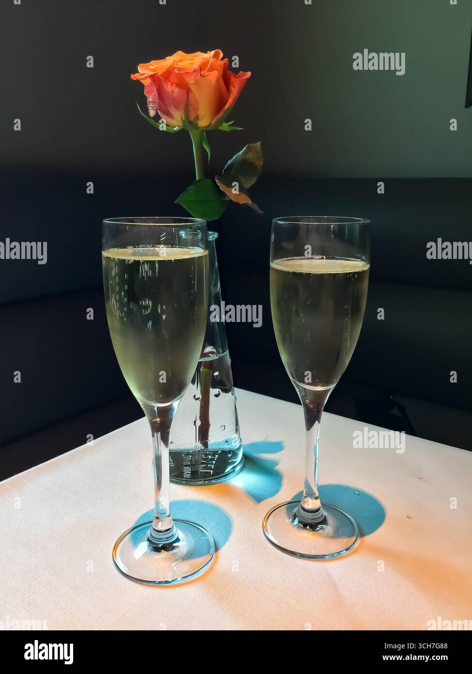 Due eleganti bicchieri di champagne e una rosa in vaso su una tovaglia bianca, simboleggiano una festa romantica. Foto Stock
