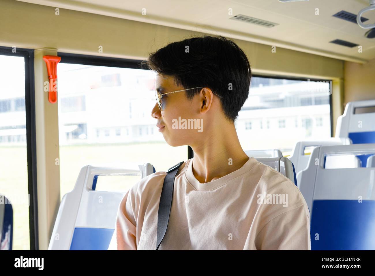 Giovane uomo con occhiali da sole, autobus che guarda fuori dal finestrino, atmosfera e stile di viaggio rilassati Foto Stock
