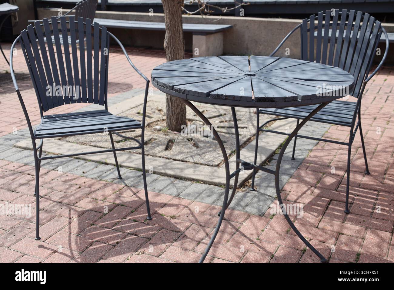 sedie da patio in legno grigio (grigio) e ferro da stiro e tavolo sul patio in pietra di pavimentazione al sole Foto Stock