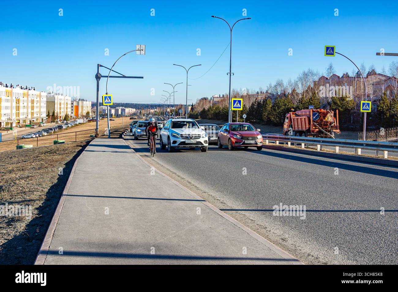 Kemerovo, Russia 17 aprile 2024. Un ciclista con equipaggiamento protettivo corre lungo una strada pubblica con auto sotto un cielo blu limpido, concentrandosi selettivamente sul cy Foto Stock