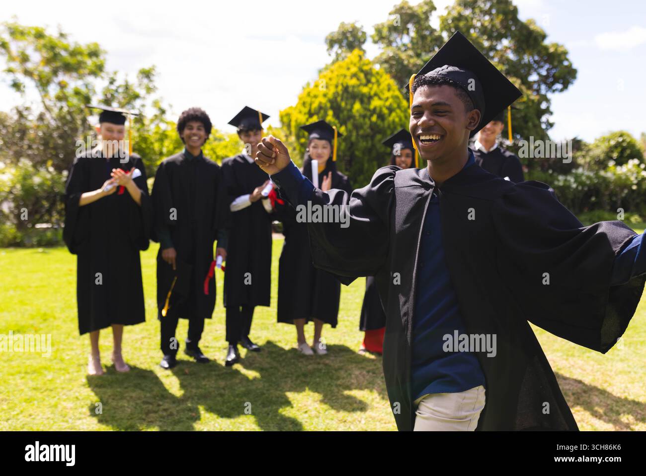 Adolescente che festeggia la laurea in giardino con amici diversi che applaudono e sorridono sullo sfondo Foto Stock