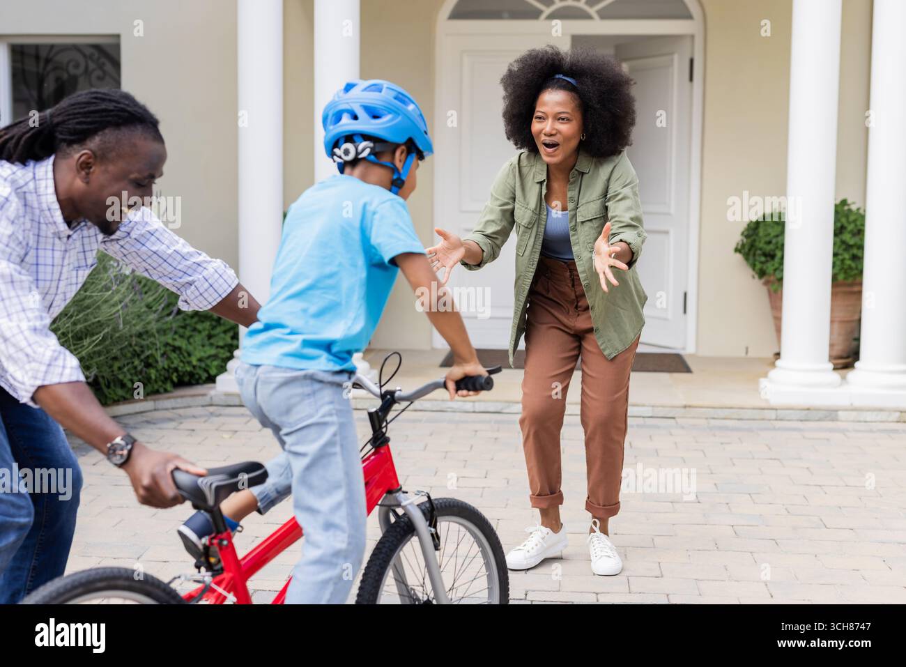 Genitori afroamericani che insegnano al figlio di andare in bicicletta, esultando con entusiasmo Foto Stock