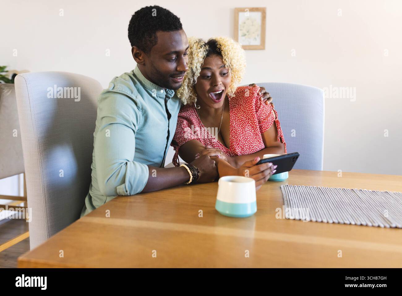 Seduti a coppie diverse utilizzando lo smartphone al tavolo da pranzo in legno a casa, con tazza in ceramica Foto Stock