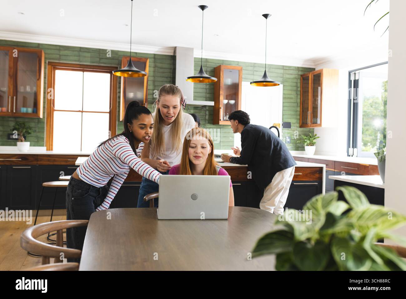 Nella cucina moderna, gli amici adolescenti collaborano con un notebook, concentrandosi sul lavoro di squadra Foto Stock