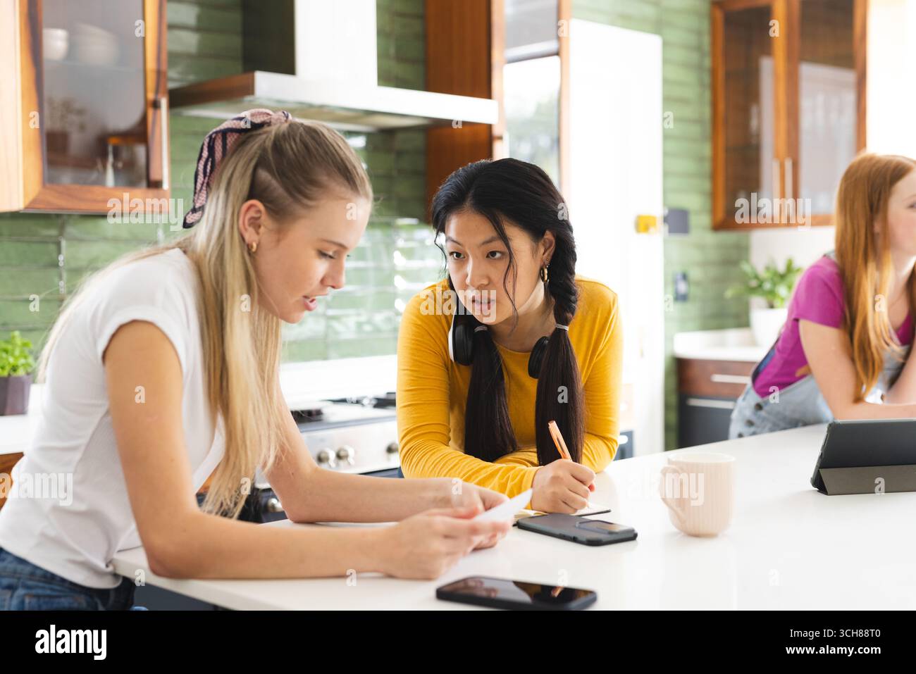Studiando insieme al bancone della cucina, ragazze adolescenti che si concentrano sulla discussione sul lavoro scolastico Foto Stock