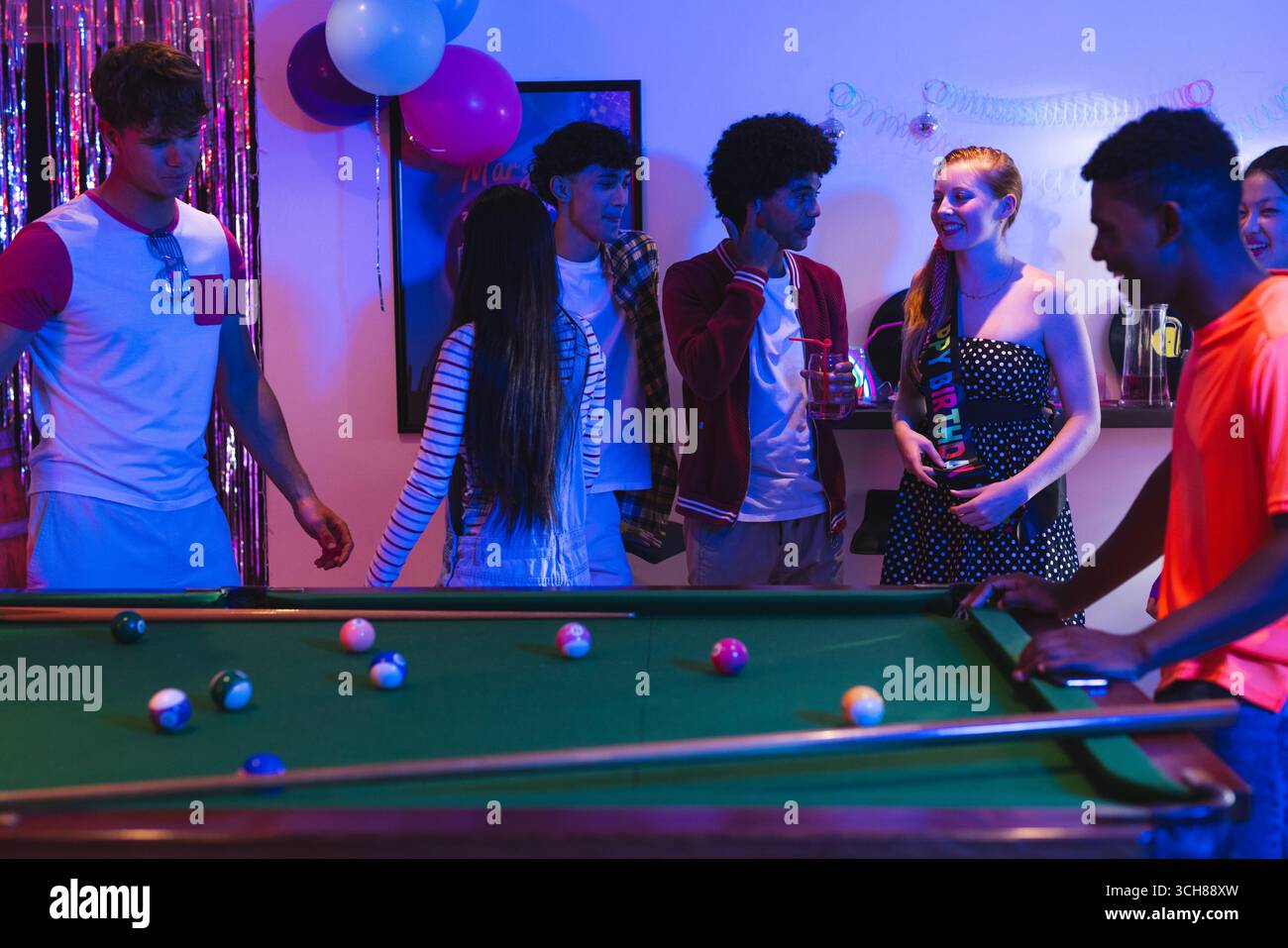 Gli adolescenti si divertono a giocare a biliardo durante una festa in casa con decorazioni colorate Foto Stock