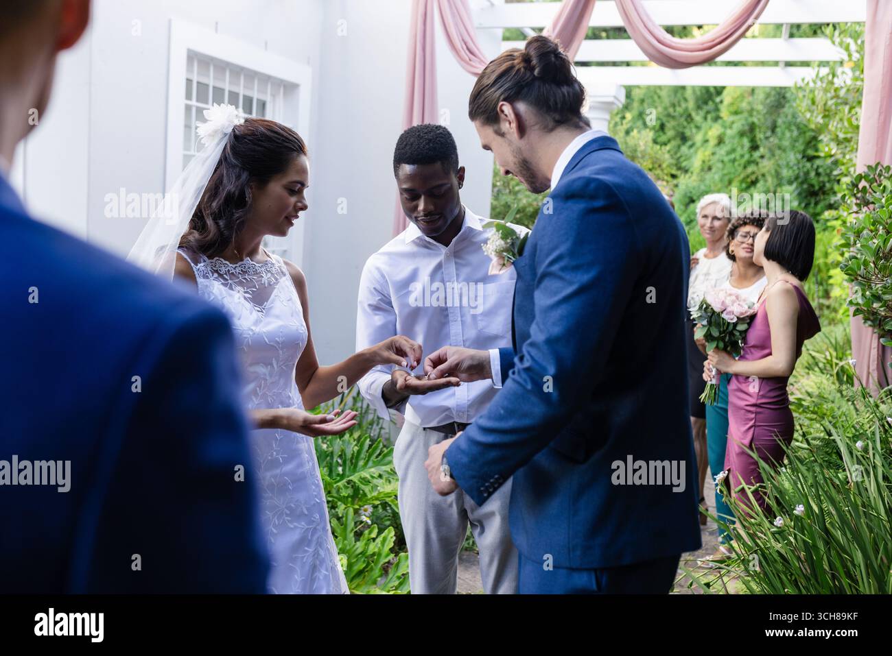 Sposa e sposo si scambiano anelli all'aperto, circondati da amici e familiari Foto Stock