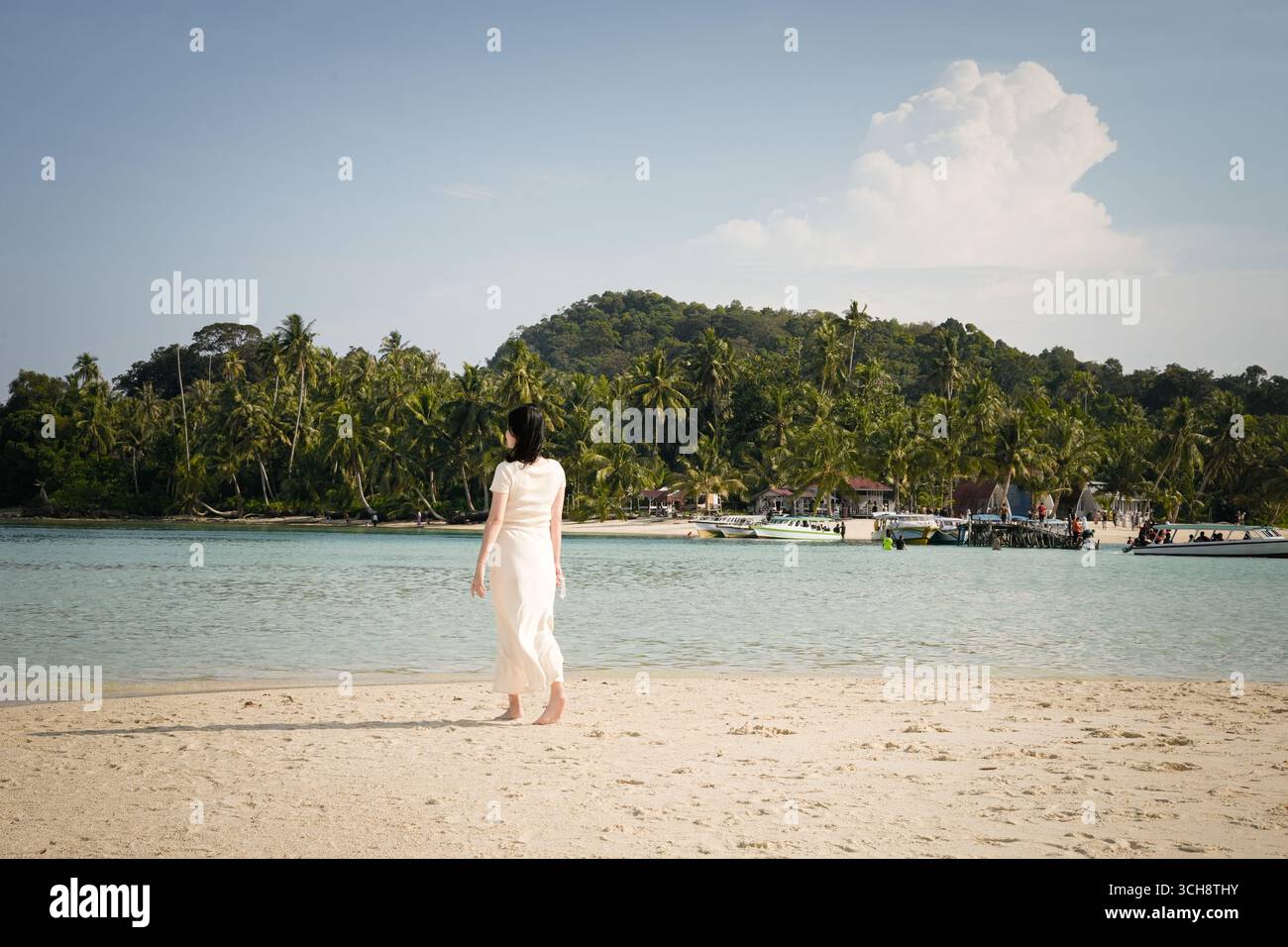 donna in un abito fluente in piedi da sola su una tranquilla spiaggia tropicale Foto Stock