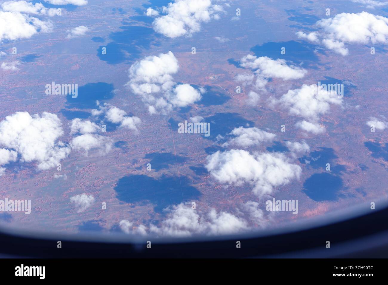 Nuvole soffici sparse bianche gettano ombre sulla terra rossa dell'Australia centrale direttamente sotto, vista dalla finestra dell'aereo. Foto Stock