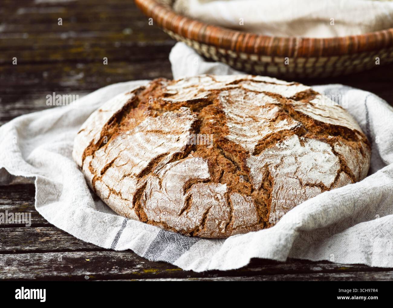 Un enorme pane rotondo con una crosta rustica e rustica poggia su un panno. Natura morta semplice e casalinga che celebra il cibo naturale e artigianale. Cibo sano fatto a mano Foto Stock