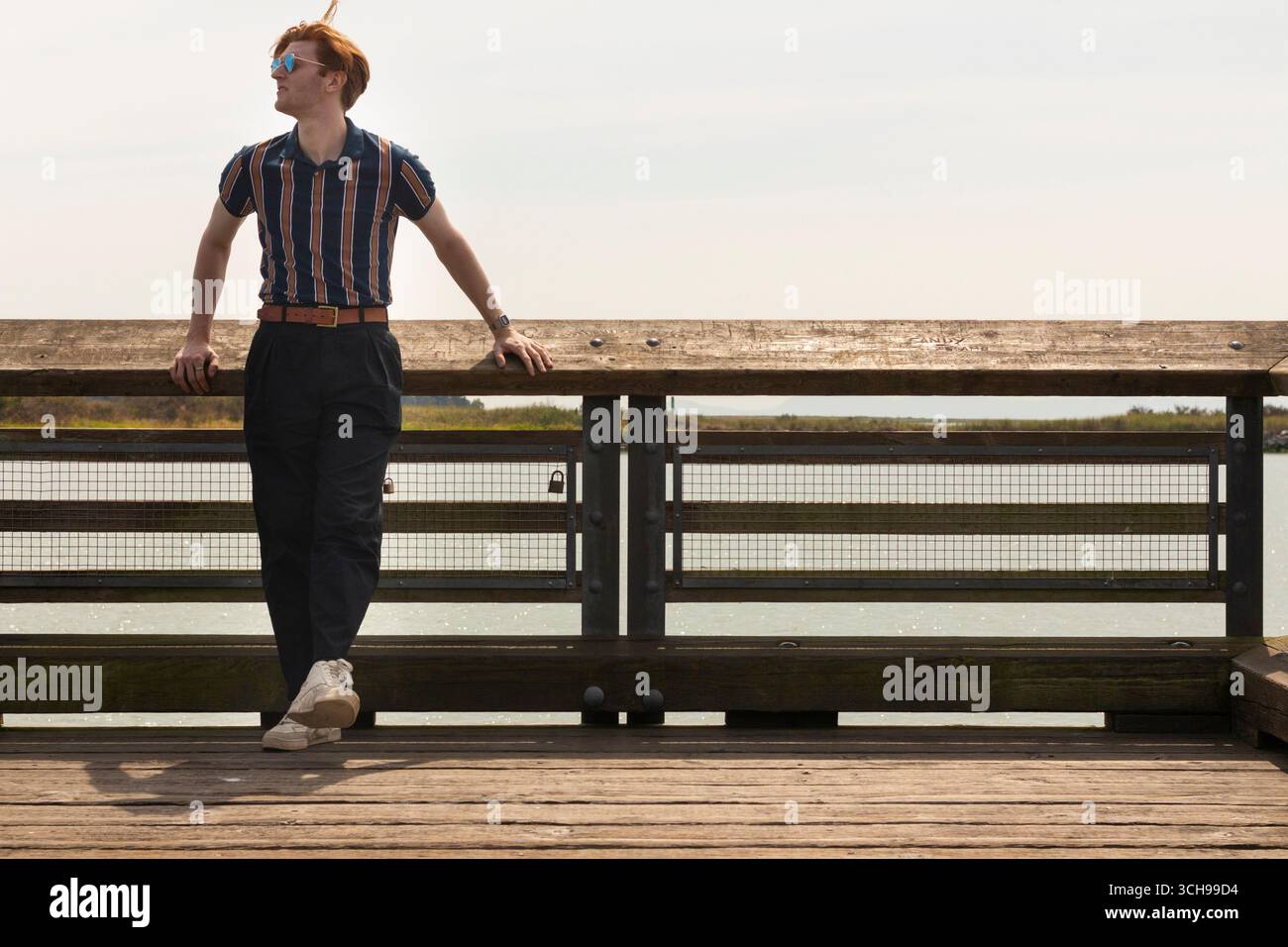 Il giovane uomo ama la giornata di sole su un molo di legno con acqua panoramica Foto Stock