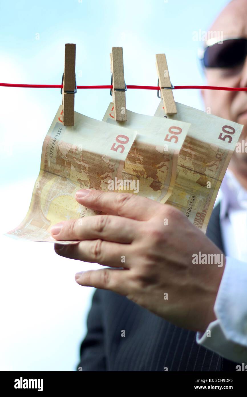 un uomo dall'aspetto sinistro afferra denaro appeso a una clothesline, utilizzabile per le crisi dell'euro, il riciclaggio di denaro, le crisi finanziarie, eccetera Foto Stock