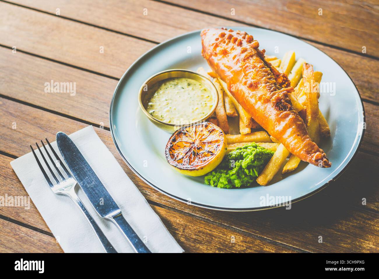 Pesce e patatine fritte alla birra, piselli moschi, salsa alla tartare e limone Foto Stock