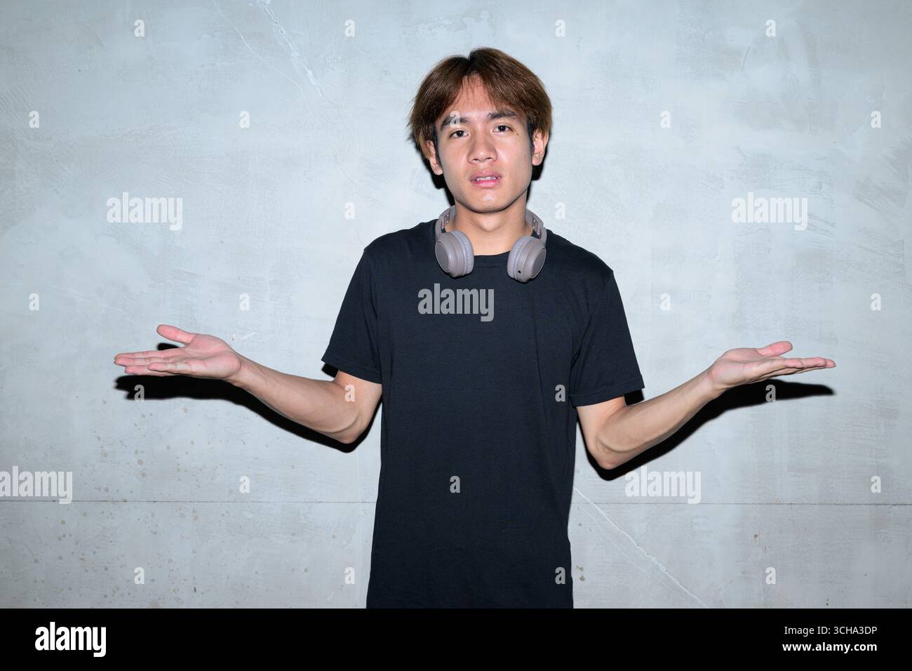 Giovane asiatico che indossa una t-shirt nera, spalle a ginocchio in un'area di costruzione minimalista in stile brutalista con pareti in cemento grigio concetto di mod Foto Stock