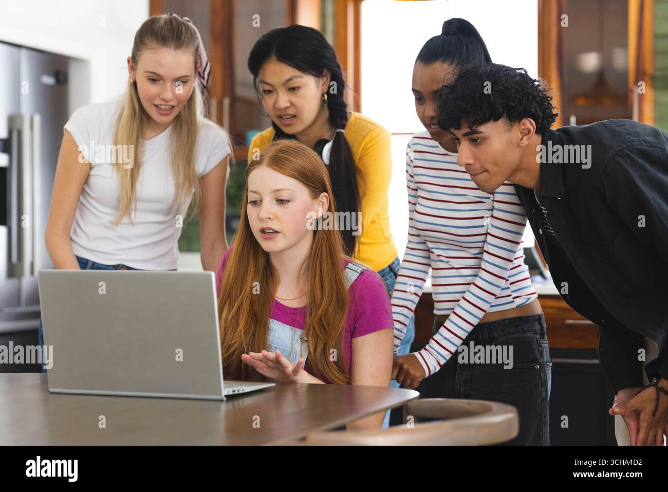 Guardare lo schermo di un notebook in cucina, i vari adolescenti che condividono momenti di gioia a casa. amici diversi, legame, tecnologia, tempo libero, felicità Foto Stock