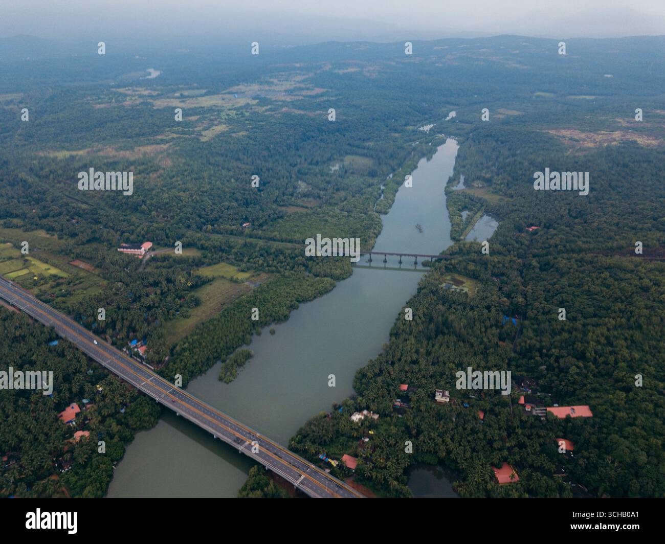 Vista aerea di un paesaggio verdeggiante dove il fiume Talpona scolpì un sentiero attraverso fitte foreste, attraversate da ponti sotto un vasto cielo, Canacona, Goa, India. Foto Stock
