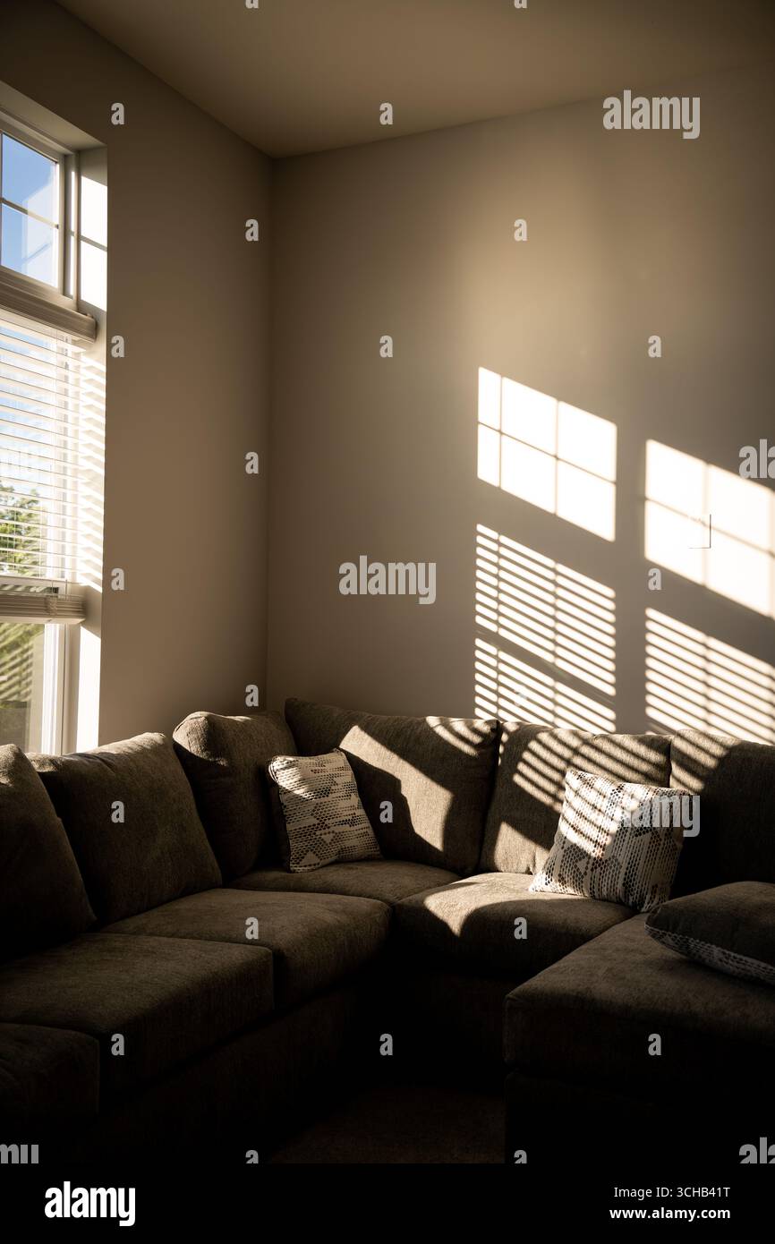 La luce del sole proietta le ombre delle finestre su un divano in un accogliente angolo salotto di una casa. Foto Stock