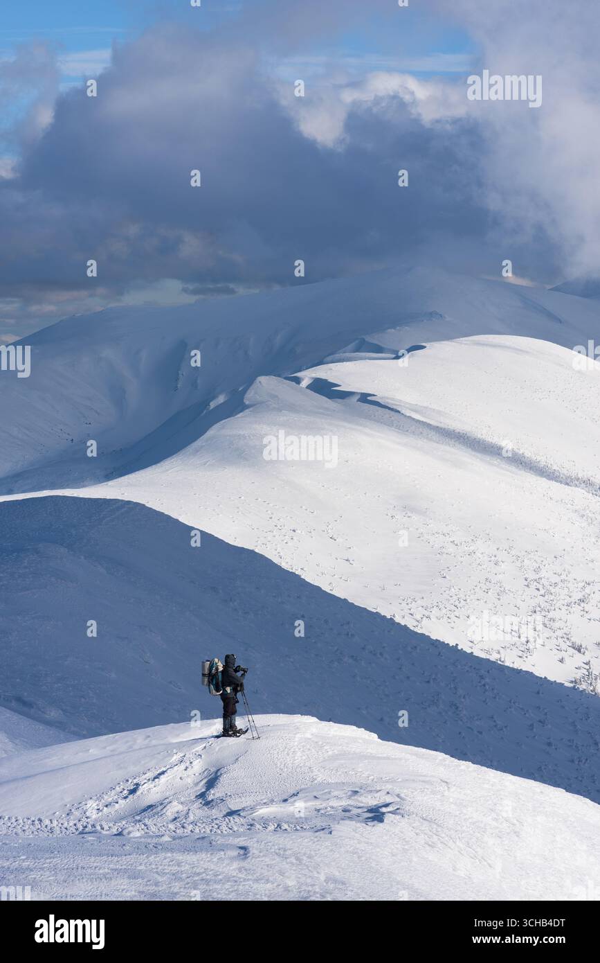 Escursionista solitario con zaino che si gode delle Snowy Mountain Ridges durante un'avventura invernale di trekking Foto Stock