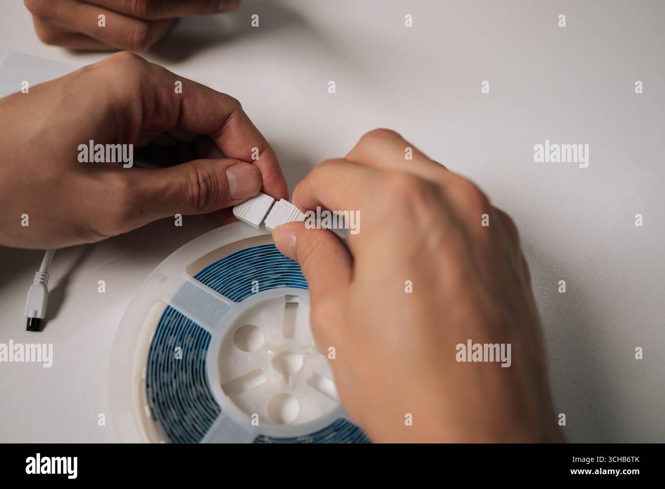 Primo piano di mani di tecnici che collegano la striscia luminosa LED RGB al connettore, preparandosi per l'installazione e mostrando componenti complessi di moderni Foto Stock