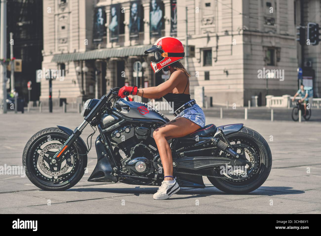 Giovane donna che posa su una motocicletta Harley personalizzata, strada urbana Foto Stock
