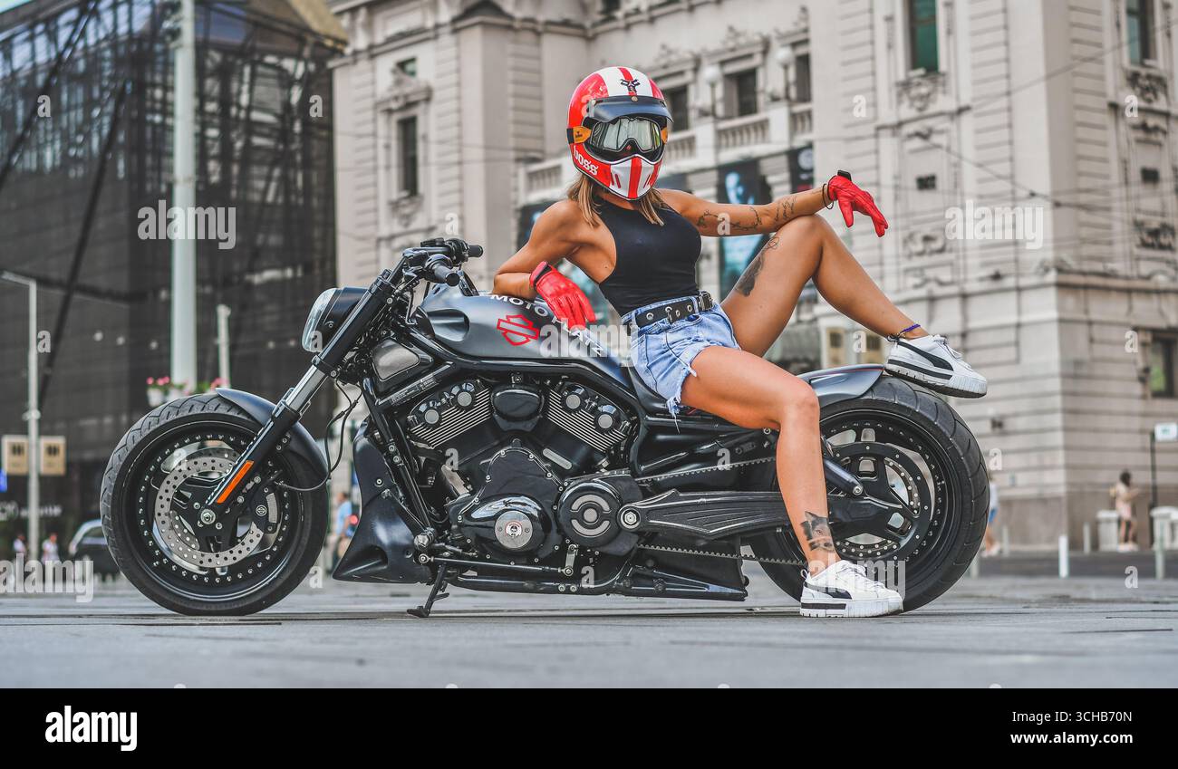 Giovane donna che posa su una motocicletta Harley personalizzata, strada urbana Foto Stock