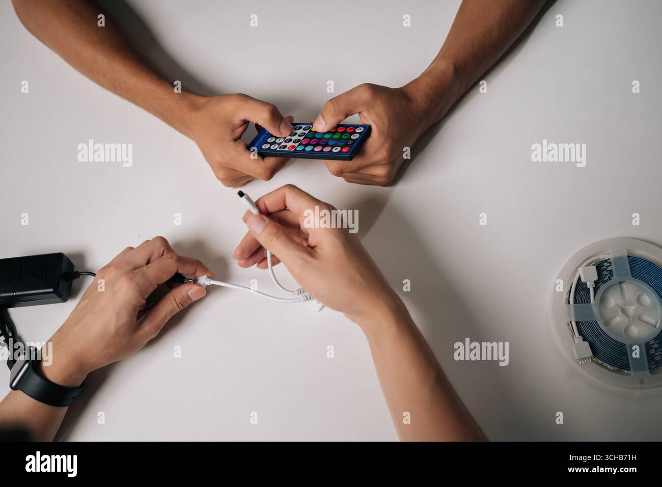 Vista dall'alto di due tecnici che collegano le strisce luminose LED RGB tramite telecomando e controller, regolando le impostazioni di retroilluminazione per personalizzarle Foto Stock