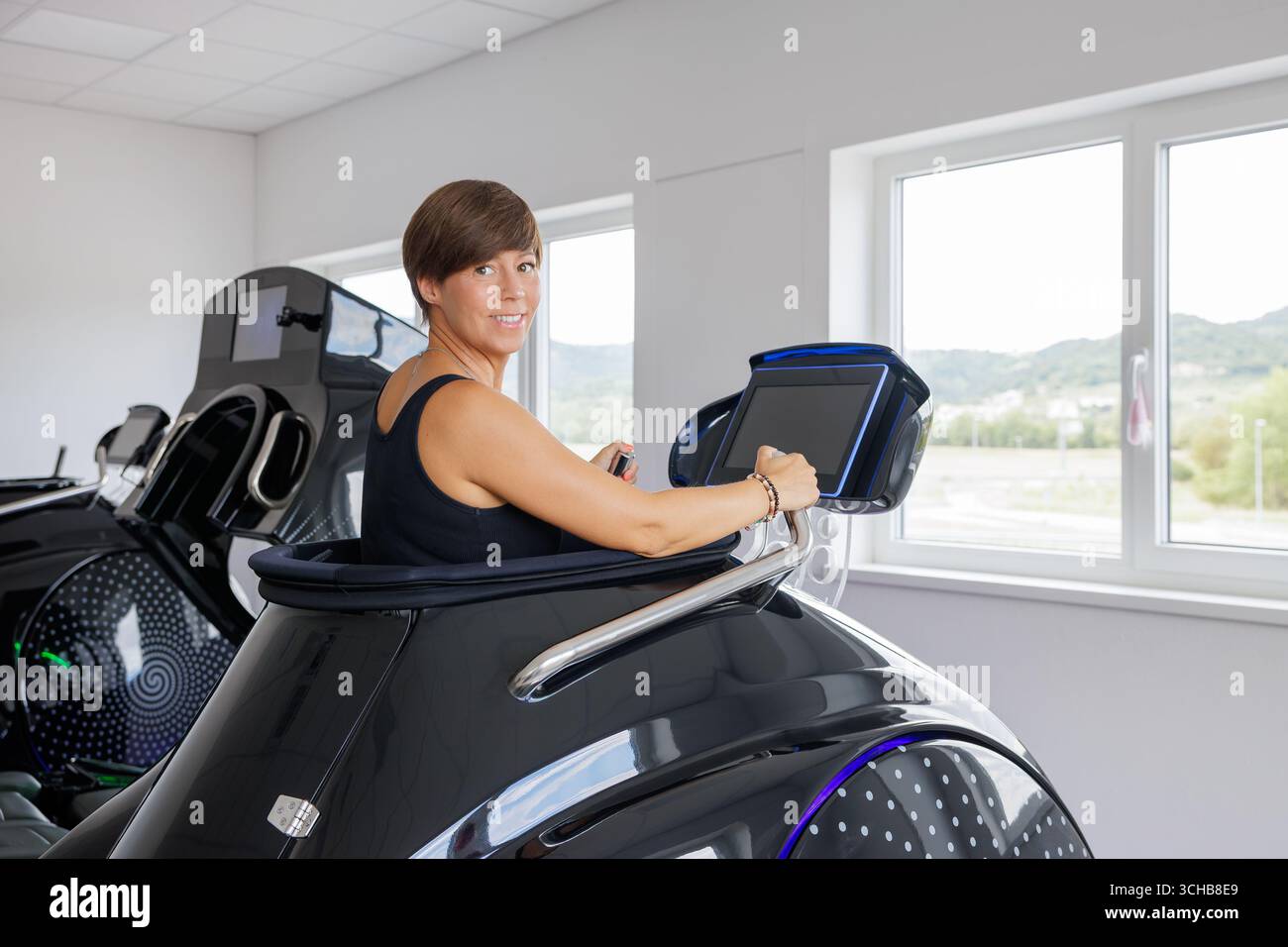 Donna sorridente all'interno della moderna capsula del tapis roulant sottovuoto con riscaldamento a infrarossi, che utilizza il touchscreen per esercizi cardiovascolari, dimagrimento e benefici per il benessere. Foto Stock