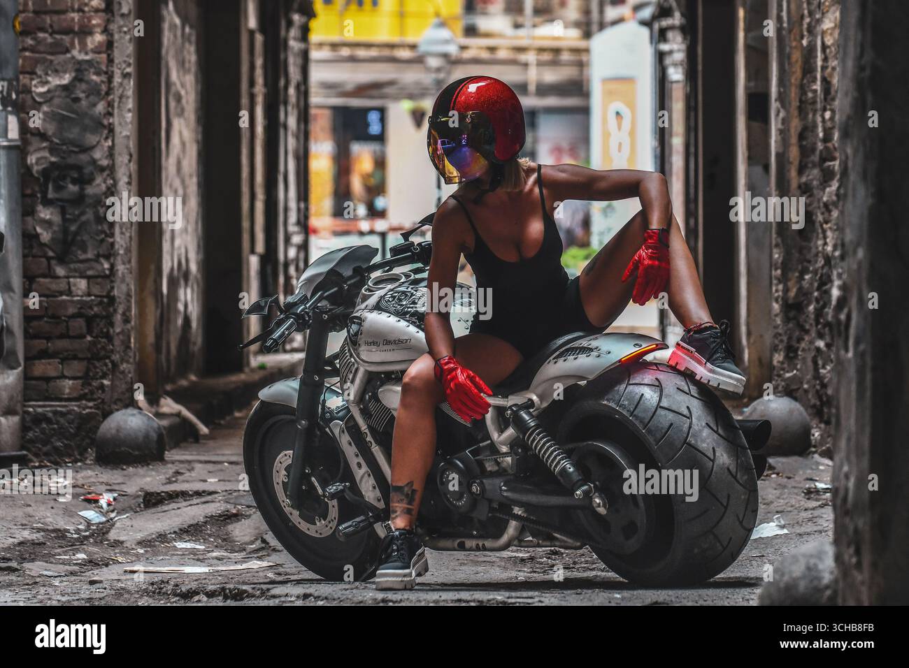 Giovane donna che posa su una motocicletta Harley personalizzata, strada urbana Foto Stock
