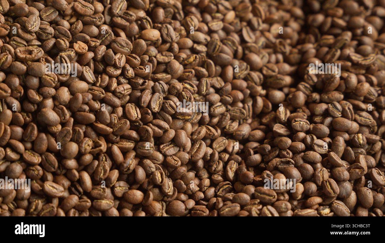 Primo piano di chicchi di caffè tostati che si mescolano nel miscelatore, frullano la macchina automatica a tamburo di metallo, mescolando la caffeina di cacao tostato presso lo stabilimento di produzione Foto Stock