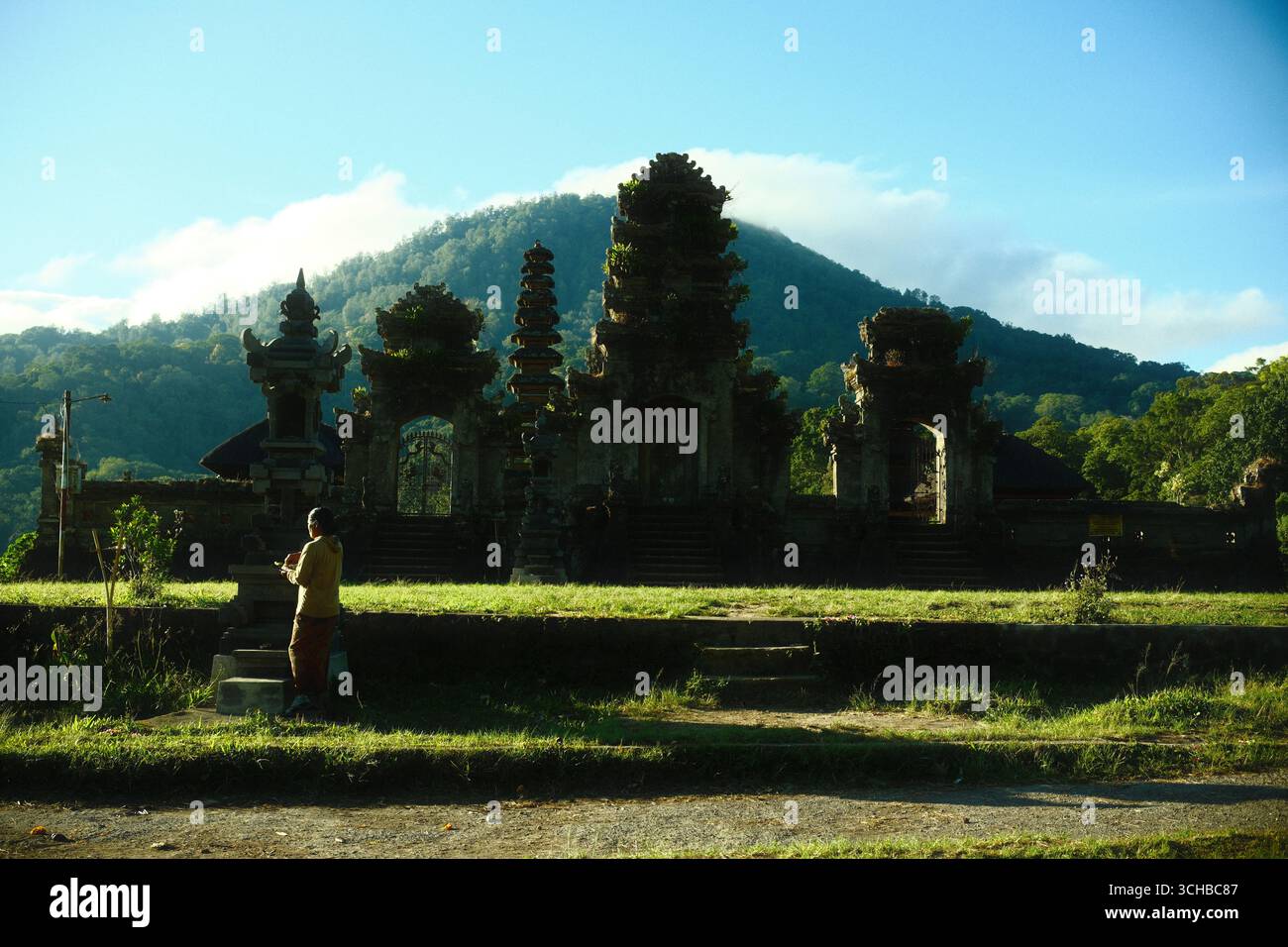 Buleleng, Bali, Indonesia - 29 agosto 2025: Una donna balinese sta pregando in un antico tempio balinese con lo sfondo di una montagna all'alba Foto Stock