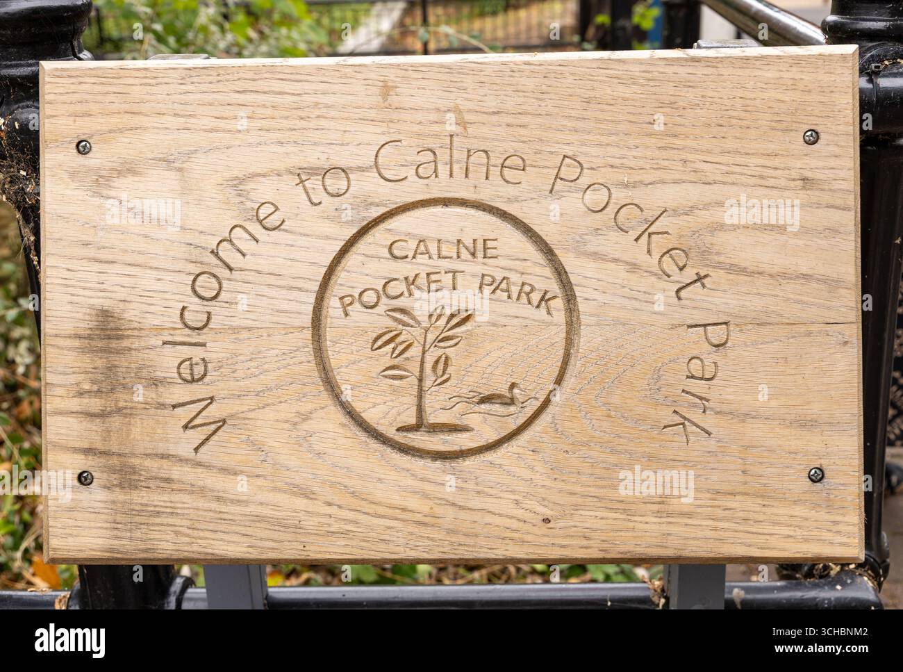 Un cartello in legno che accoglie i visitatori al Calne Pocket Park con testo inciso e un design decorativo che simboleggia la natura Foto Stock