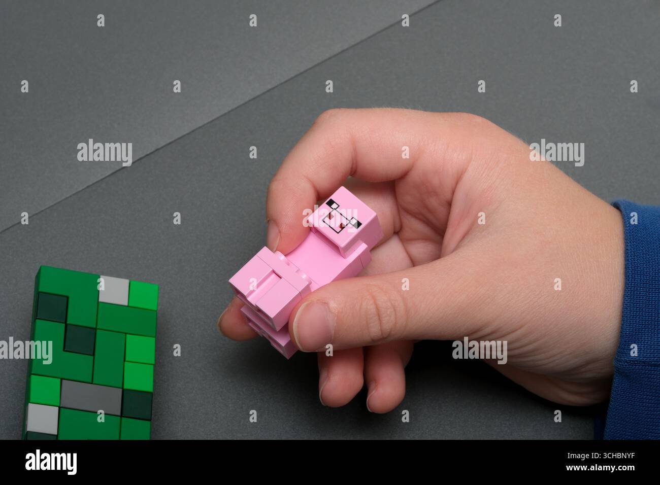 La mano di un bambino costruisce sapientemente un modello di animale rosa a partire da blocchi colorati su un tavolo. Foto Stock