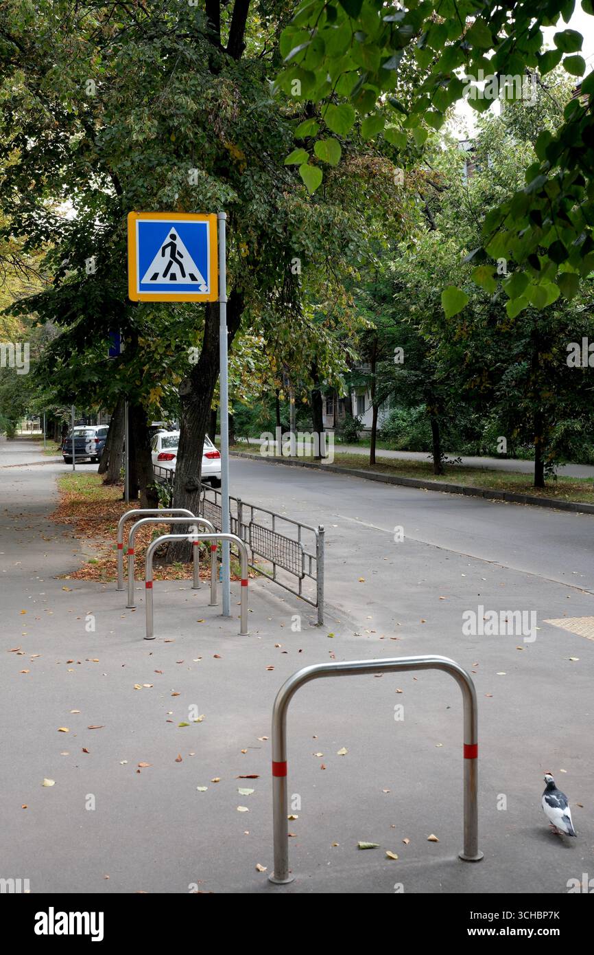 Una strada tranquilla costeggiata da alberi presenta un cartello pedonale tra foglie cadute. Foto Stock