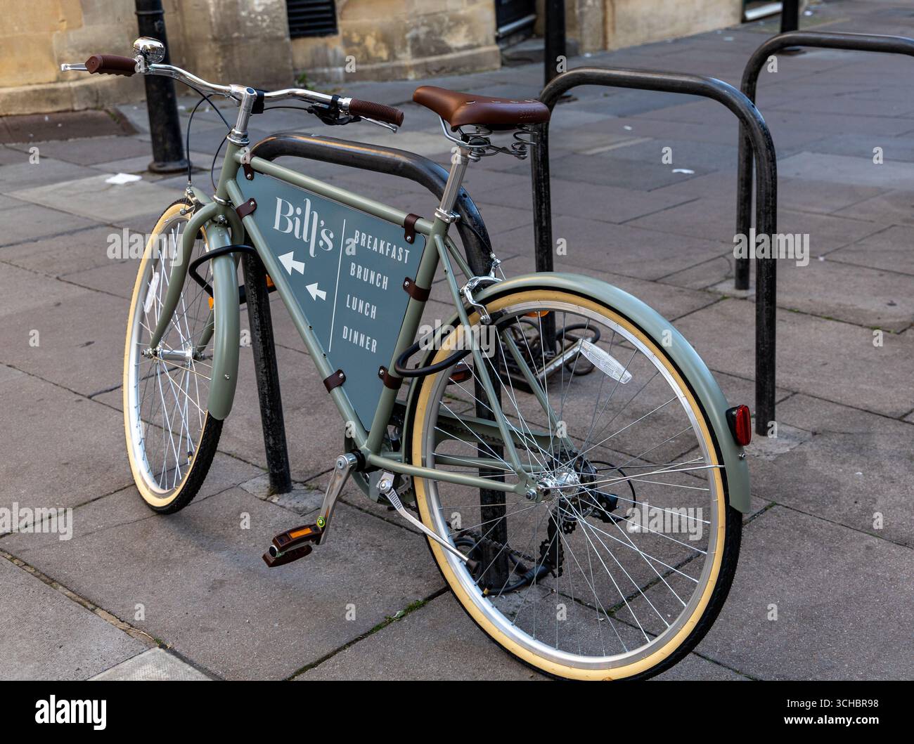 Una bicicletta in stile vintage con un pannello pubblicitario per un ristorante che offre colazione, brunch, pranzo e cena, parcheggiata su un marciapiede Bath UK Foto Stock
