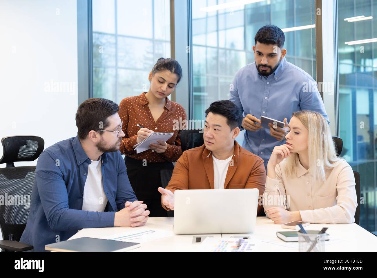 Cinque professionisti aziendali con background diversi si riuniscono intorno a un notebook. Impegnarsi attivamente in una discussione collaborativa per analizzare i dati. Strategi Foto Stock