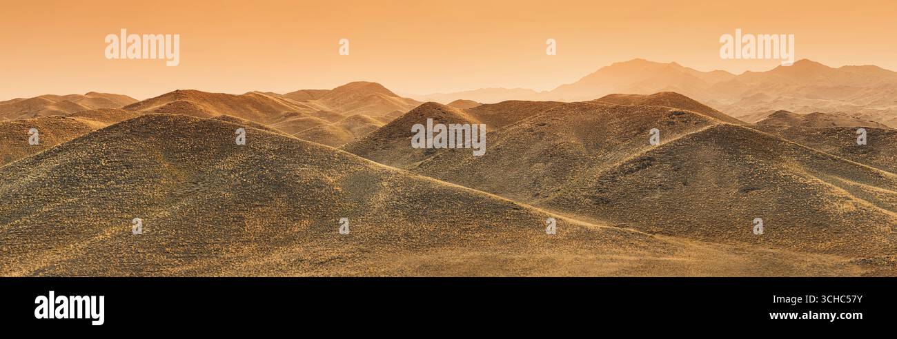 Le colline panoramiche che si estendono attraverso un vasto paesaggio desertico, caratterizzato da erba secca bagnata dal caldo bagliore del tramonto, creano una vista mozzafiato Foto Stock