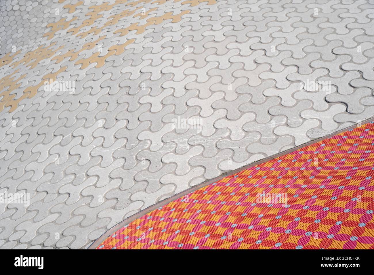 Il caratteristico motivo della pavimentazione in cemento ondulato incontra una superficie piastrellata colorata in un moderno design urbano Foto Stock