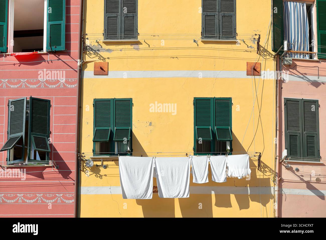 265 facciate arancioni, gialle e rosa con persiane verdi di edifici in Piazza Guglielmo Marconi, asciugatura al sole. Vernazza, Italia. Foto Stock